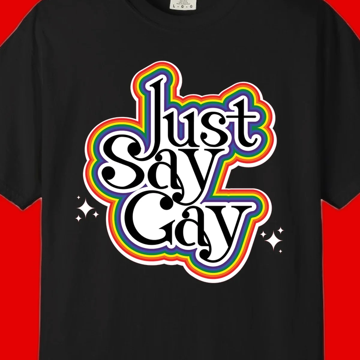 Just Say Gay Pride design with bold black text surrounded by vibrant rainbow border and sparkle accents on gray background