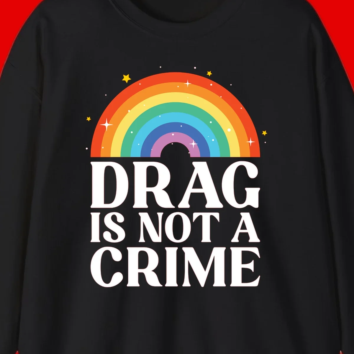 Colorful rainbow arc with stars above white text reading 'Drag Is Not A Crime' on gray background