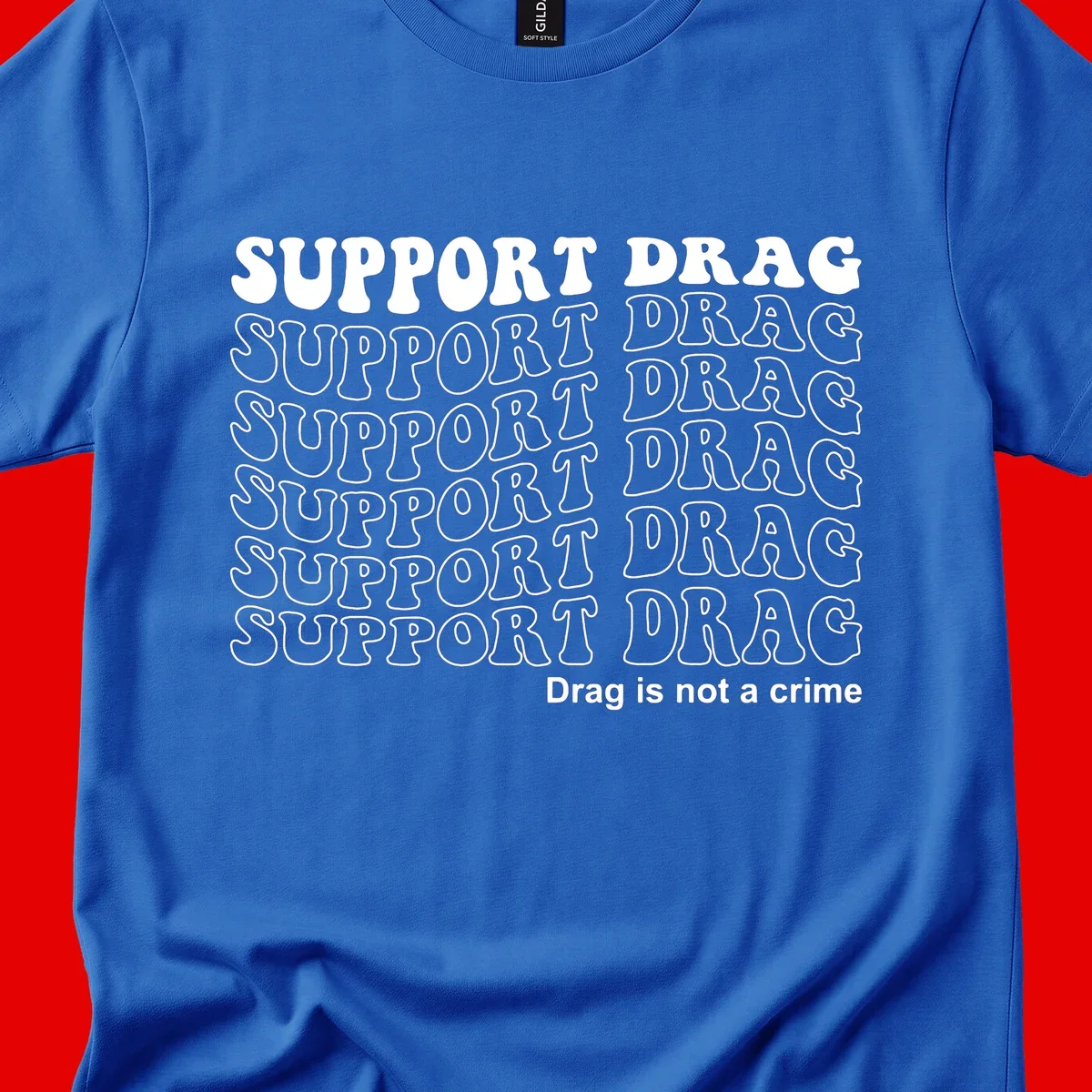 Gray t-shirt design with white text reading 'Support Drag' repeated throughout and 'Drag is not a crime' at bottom