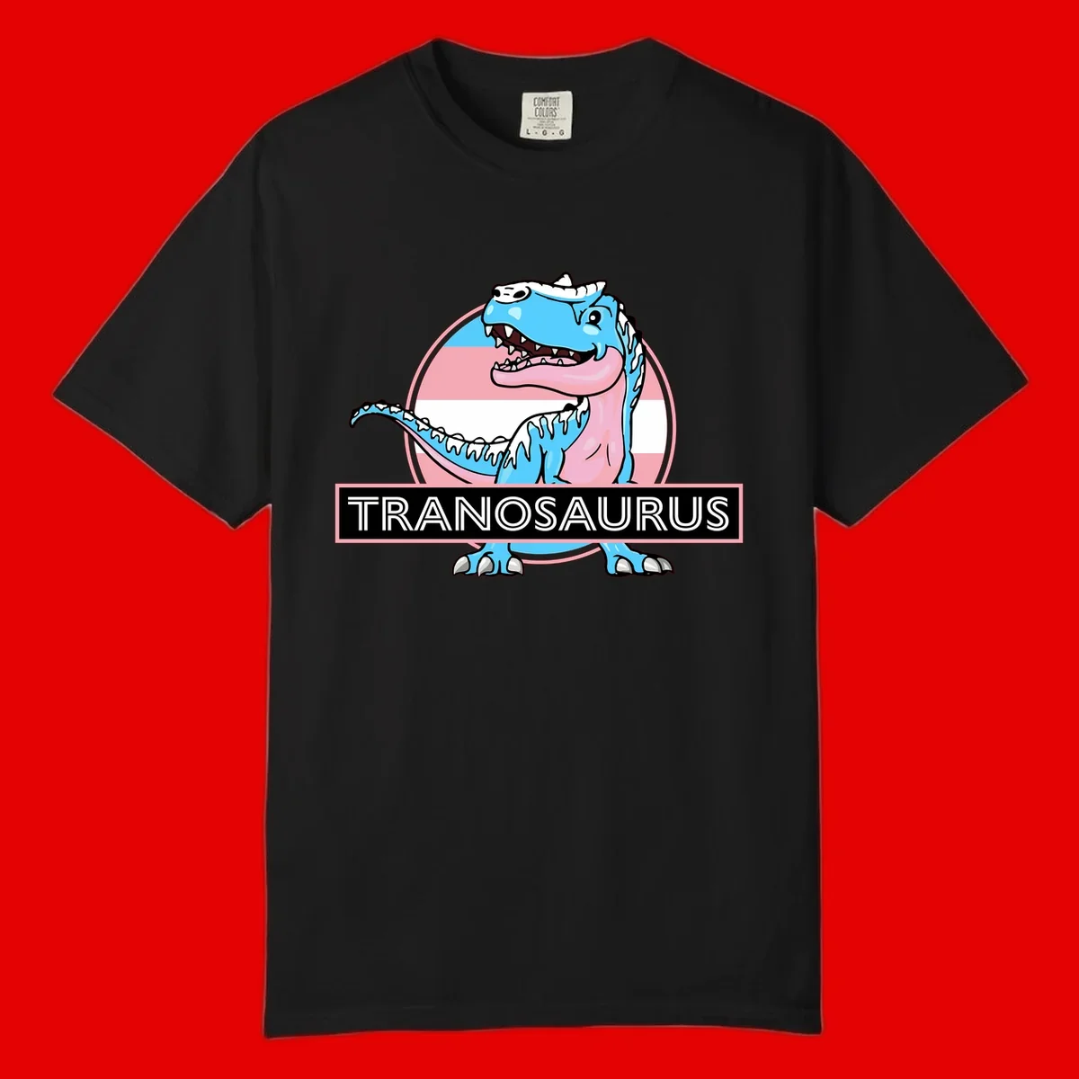 Blue cartoon T-Rex dinosaur with open mouth against pink and white pride flag circular background, labeled Tranosaurus