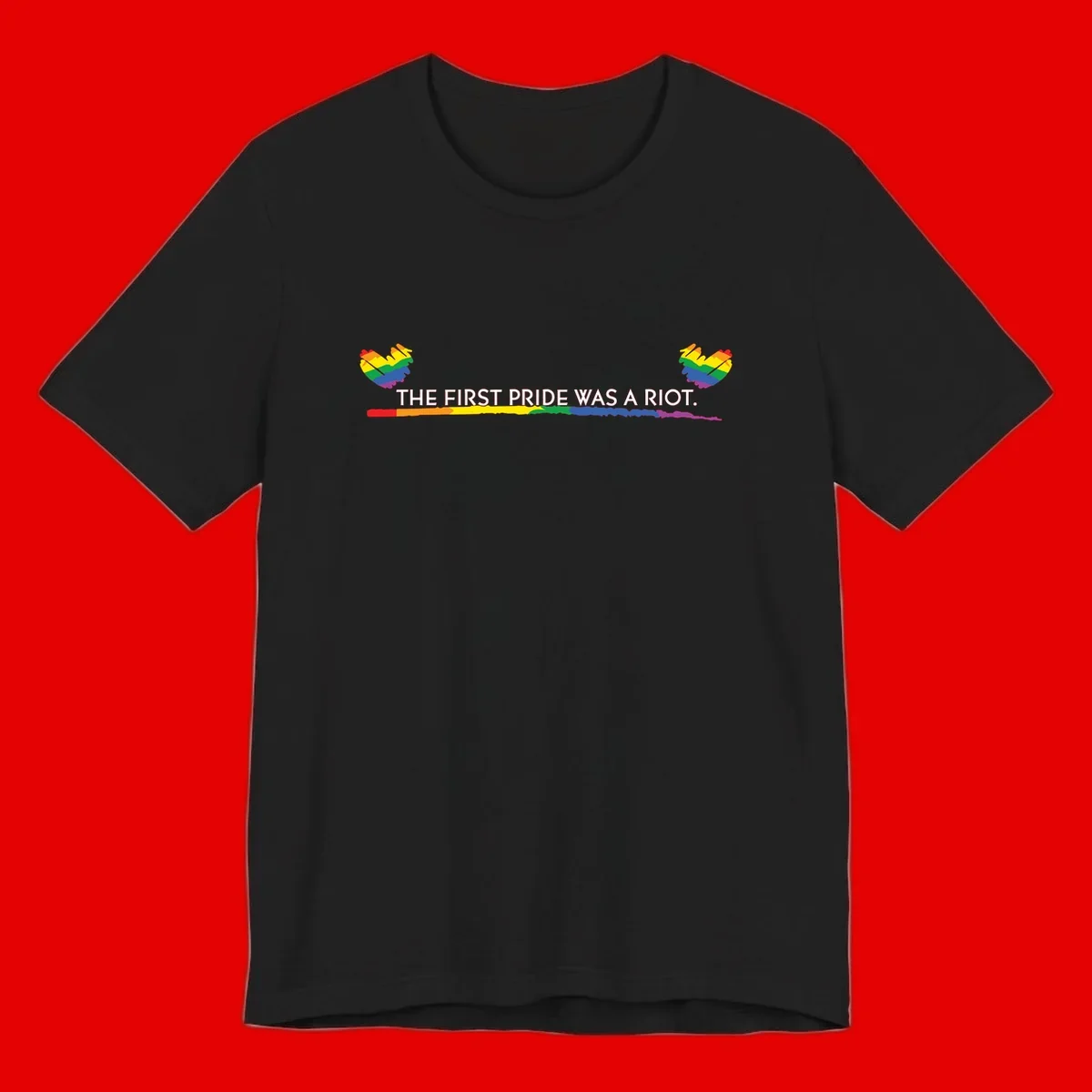 Gray background with white text reading 'THE FIRST PRIDE WAS A RIOT' surrounded by rainbow pride hearts and gradient stripe