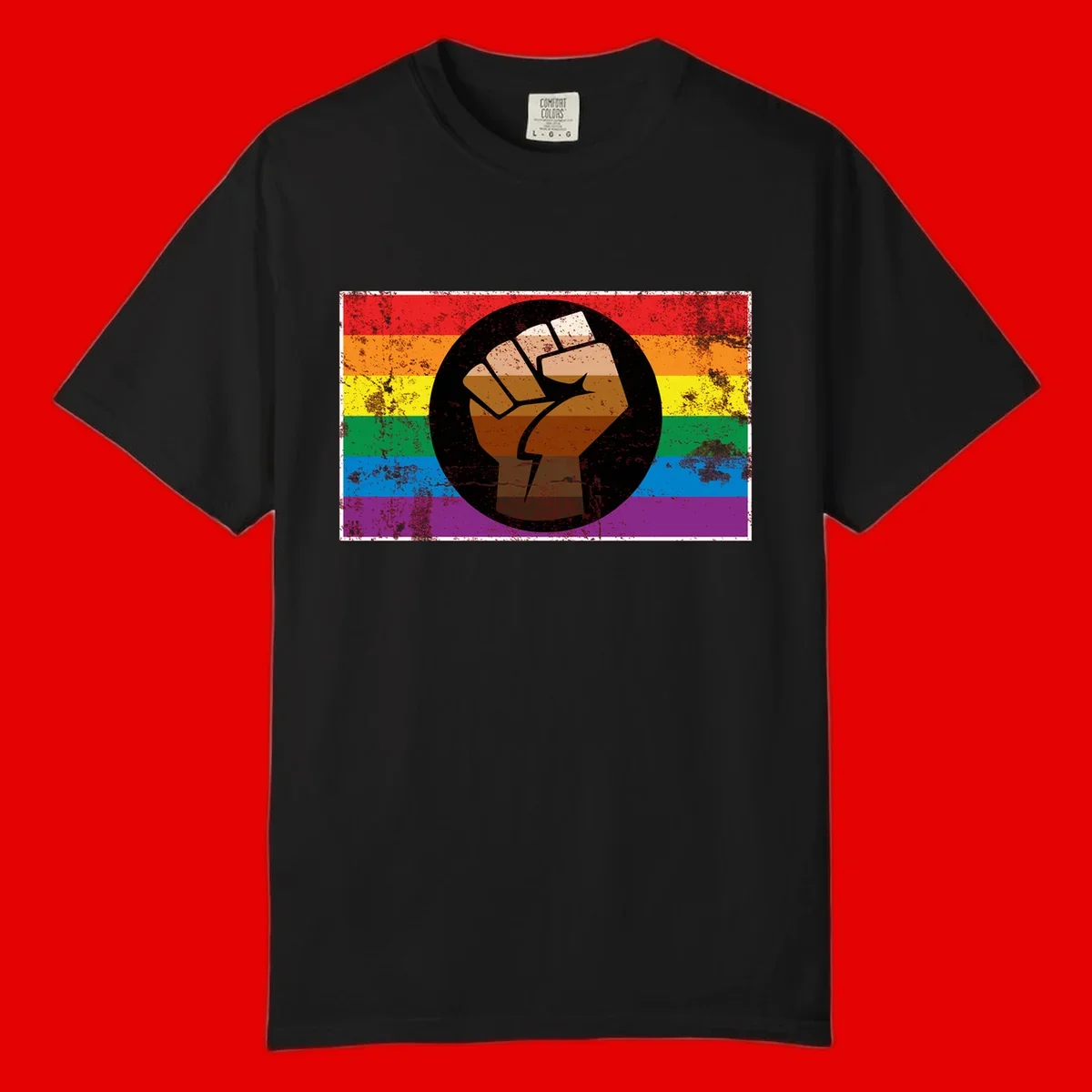 Distressed circular badge featuring a raised brown fist overlaid on a rainbow pride flag background, symbolizing LGBTQ+ solidarity and empowerment