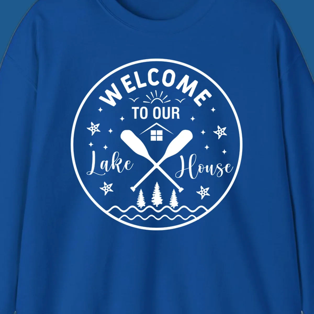 Welcome to our lake house circular design with oars, house, trees, and text.