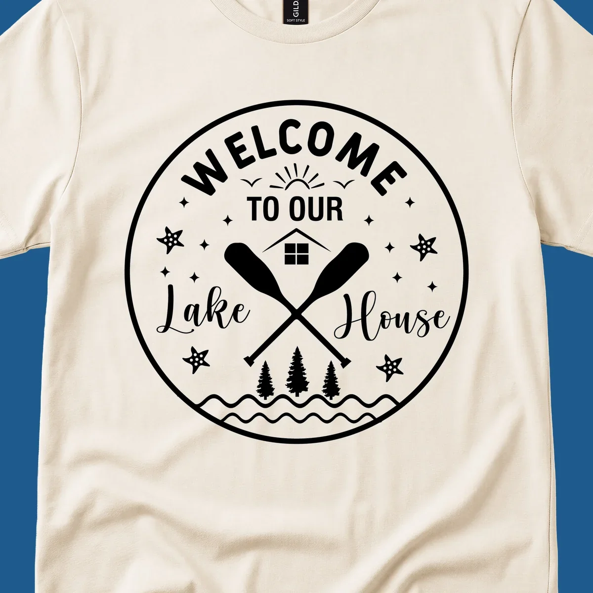 Welcome to our lake house circular design with oars, house, trees, and text.