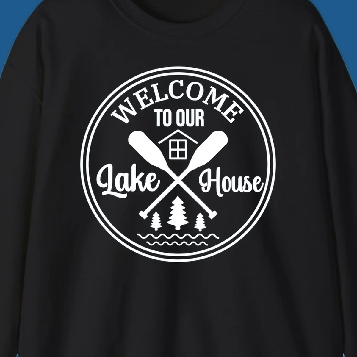Circular badge design with text 'WELCOME TO OUR Lake House', crossed oars, house, trees, and waves.