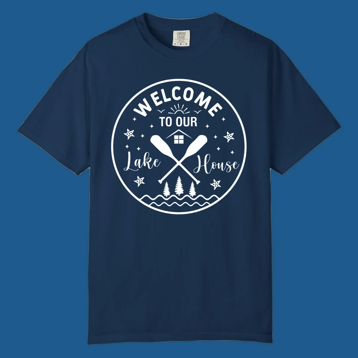 Welcome to our lake house circular design with oars, house, trees, and text.