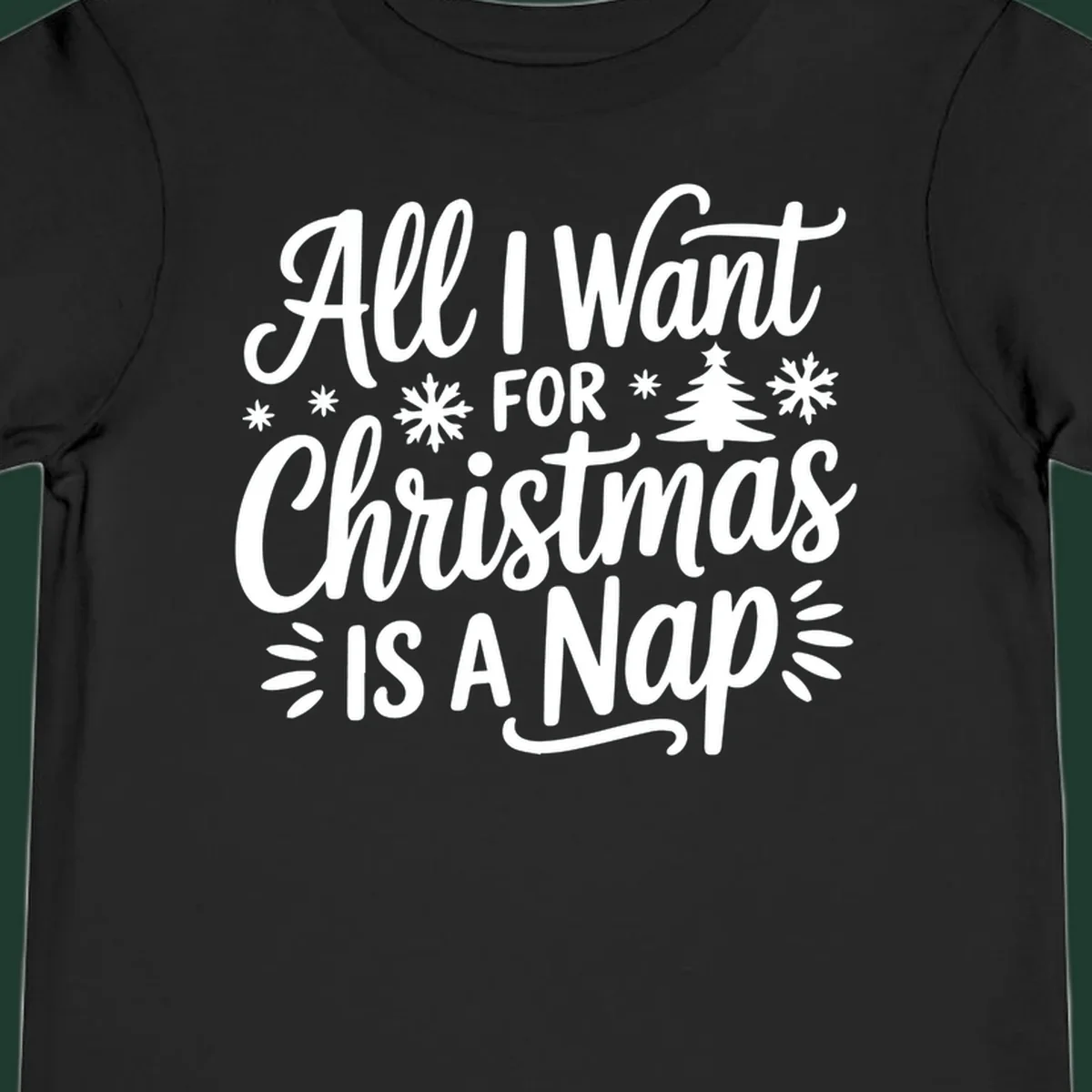 All I Want For Christmas Is A Nap typographic design with snowflakes and a Christmas tree.
