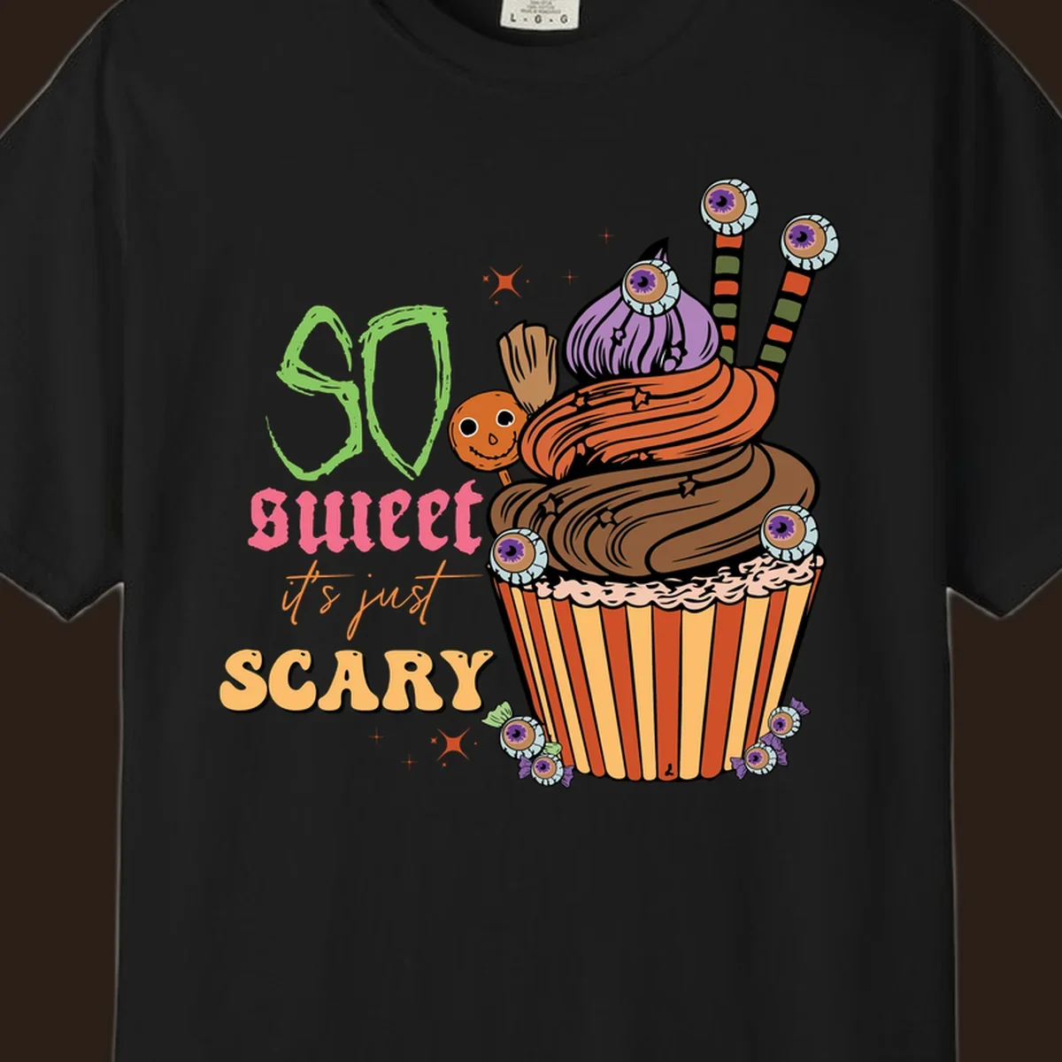 Halloween cupcake illustration with text 'So Sweet It's Just Scary', featuring candy eyeballs and a ghost lollipop.
