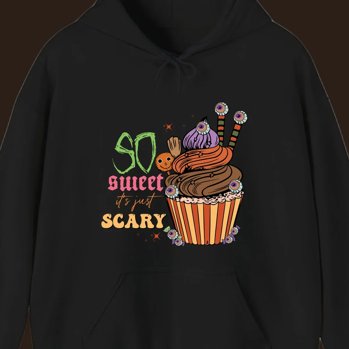 Halloween cupcake illustration with text 'So Sweet It's Just Scary', featuring candy eyeballs and a ghost lollipop.