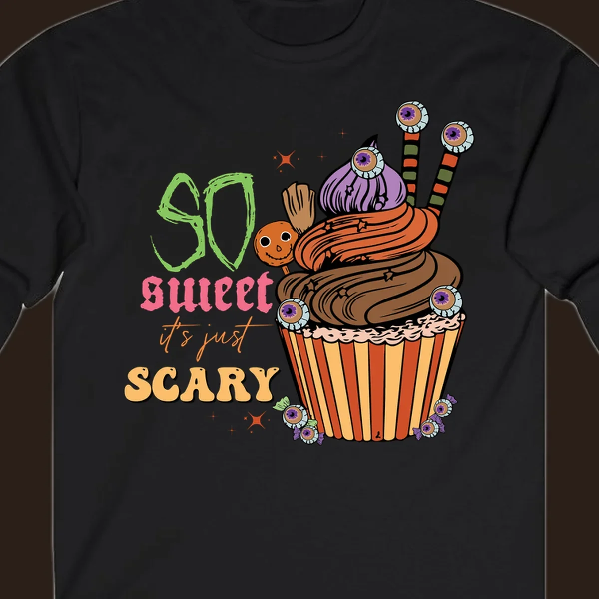 Halloween cupcake illustration with text 'So Sweet It's Just Scary', featuring candy eyeballs and a ghost lollipop.