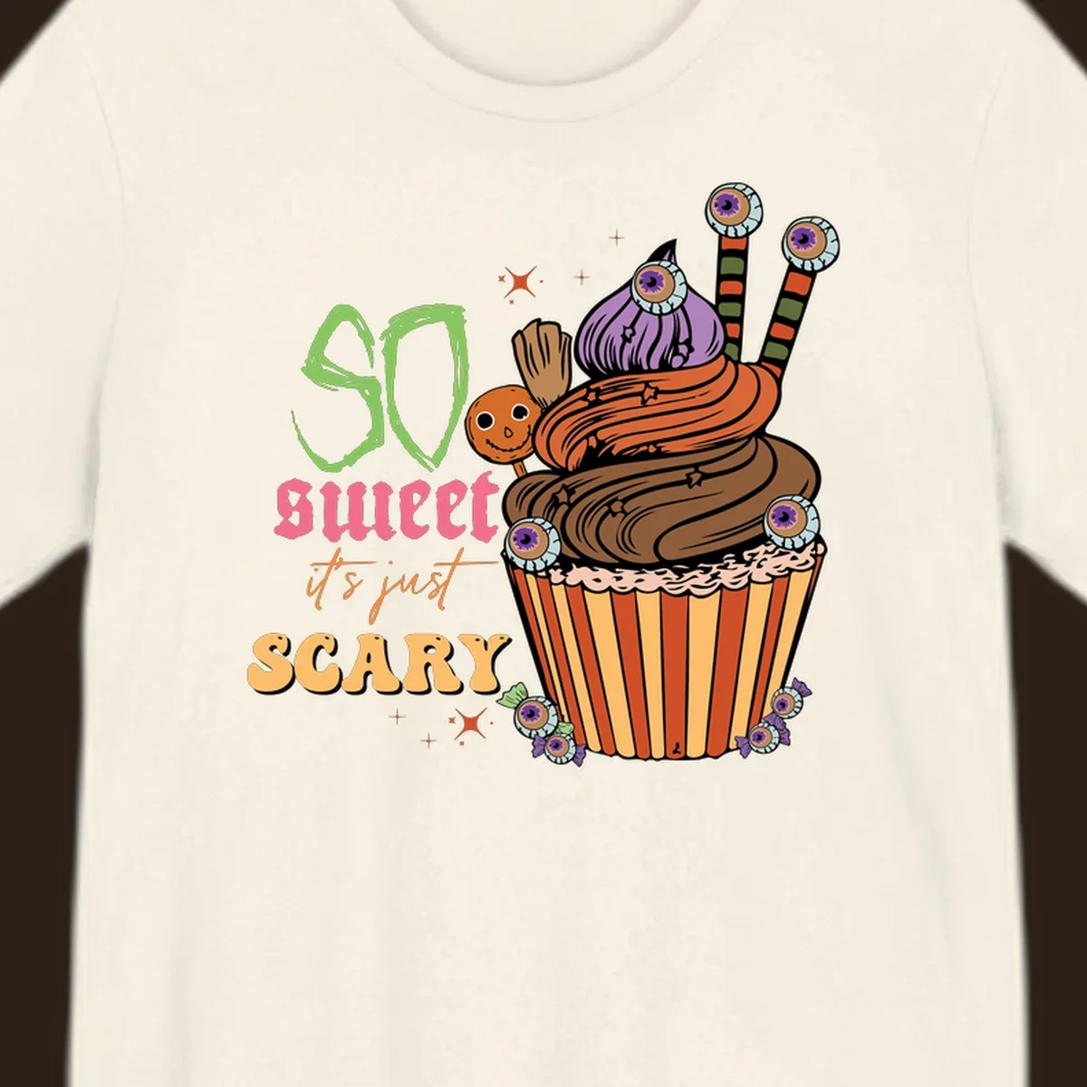 Halloween cupcake illustration with text 'So Sweet It's Just Scary', featuring candy eyeballs and a ghost lollipop.