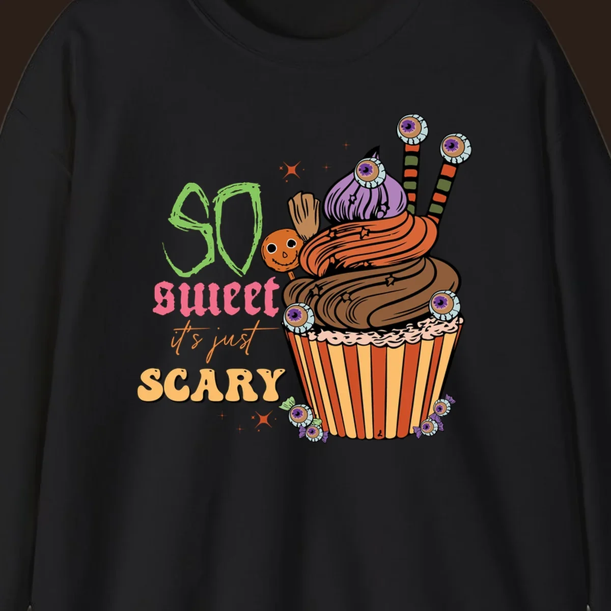 Halloween cupcake illustration with text 'So Sweet It's Just Scary', featuring candy eyeballs and a ghost lollipop.