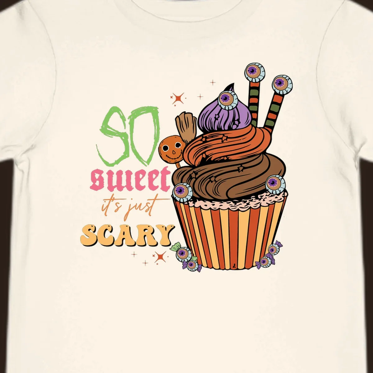 Halloween cupcake illustration with text 'So Sweet It's Just Scary', featuring candy eyeballs and a ghost lollipop.