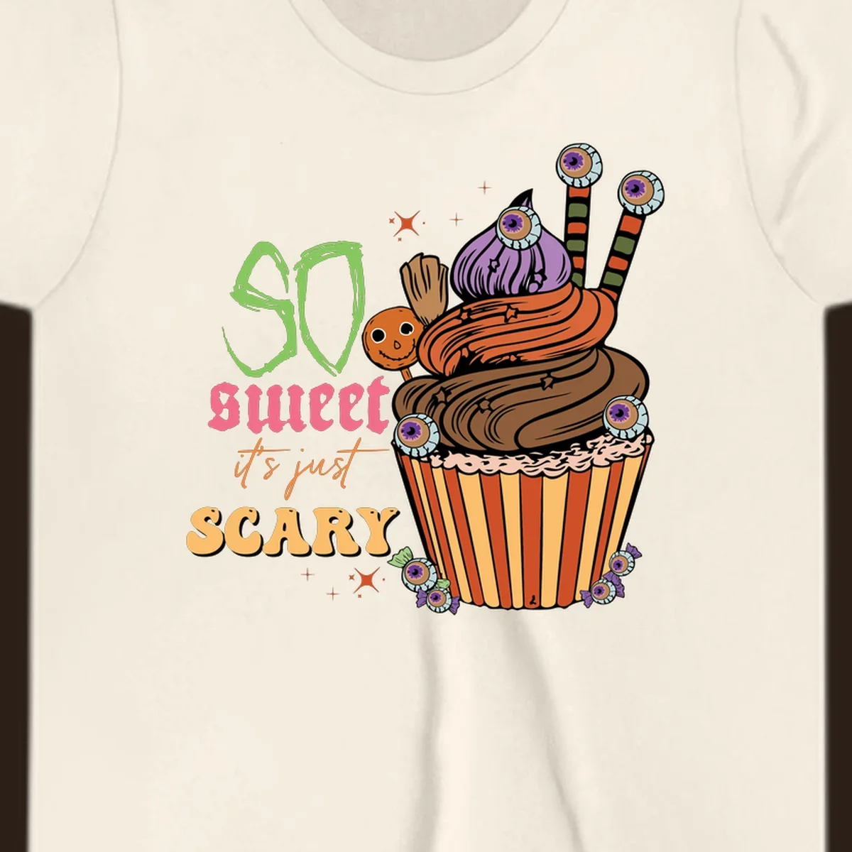 Halloween cupcake illustration with text 'So Sweet It's Just Scary', featuring candy eyeballs and a ghost lollipop.