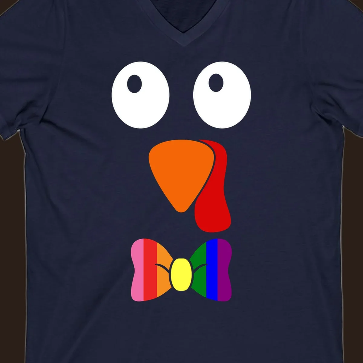 Cartoon turkey face with rainbow bowtie, featuring large eyes, orange beak, and red wattle. Thanksgiving holiday graphic.