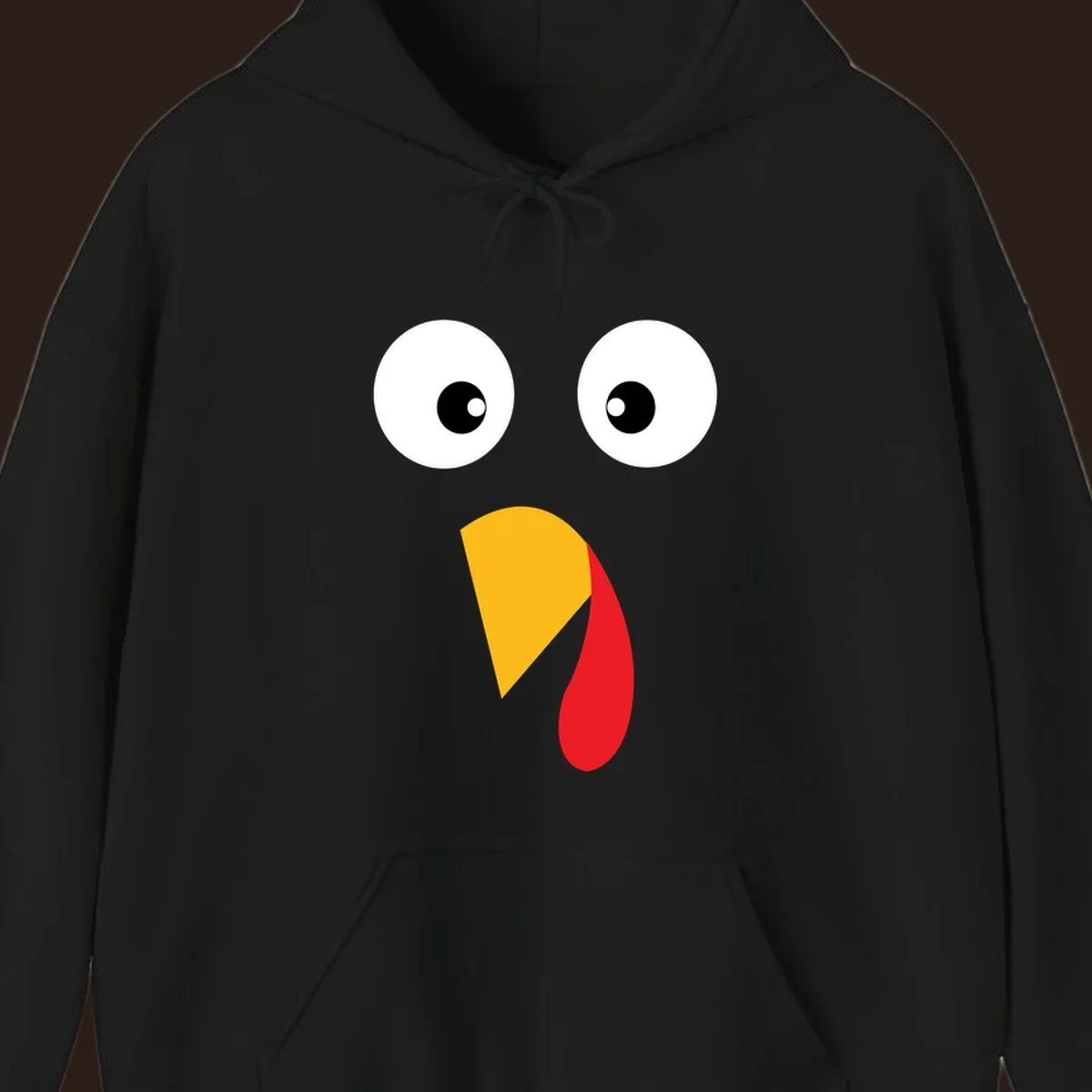 Googly eyed turkey face illustration with yellow beak and red wattle on black background.
