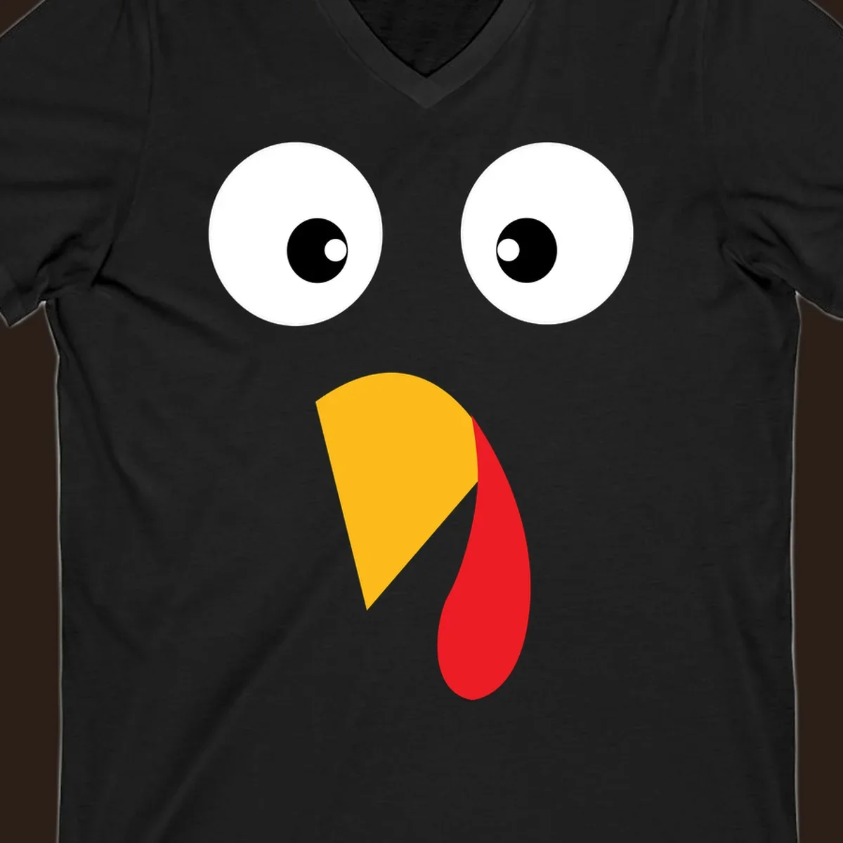 Googly eyed turkey face illustration with yellow beak and red wattle on black background.