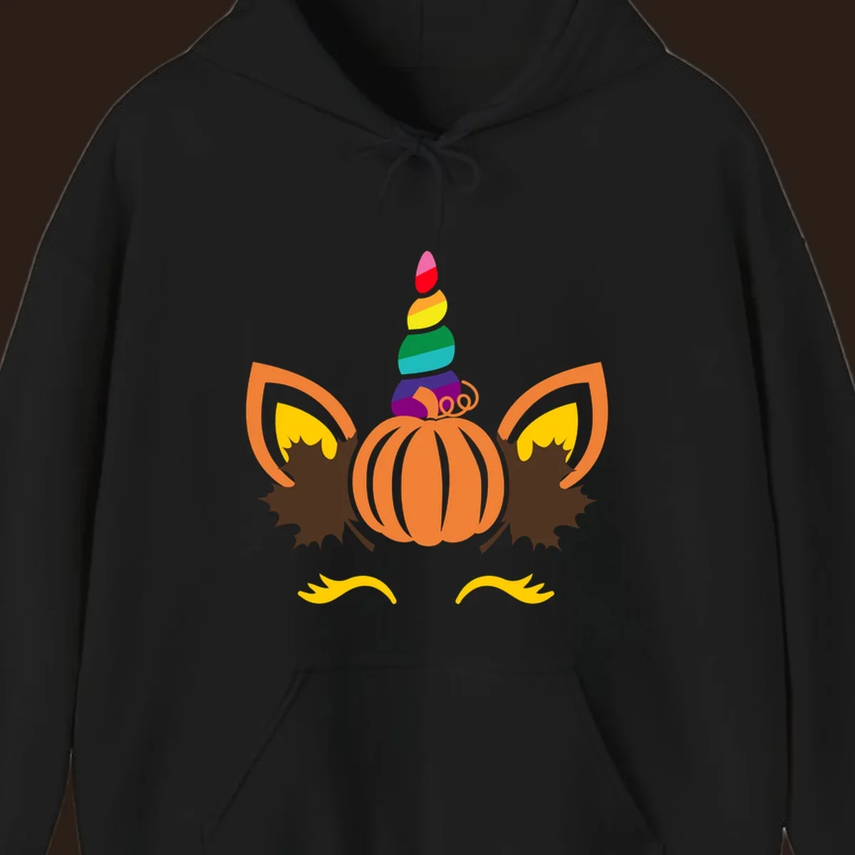 Illustration of a unicorn face made from a pumpkin with a rainbow horn and autumn leaves, on a black background.