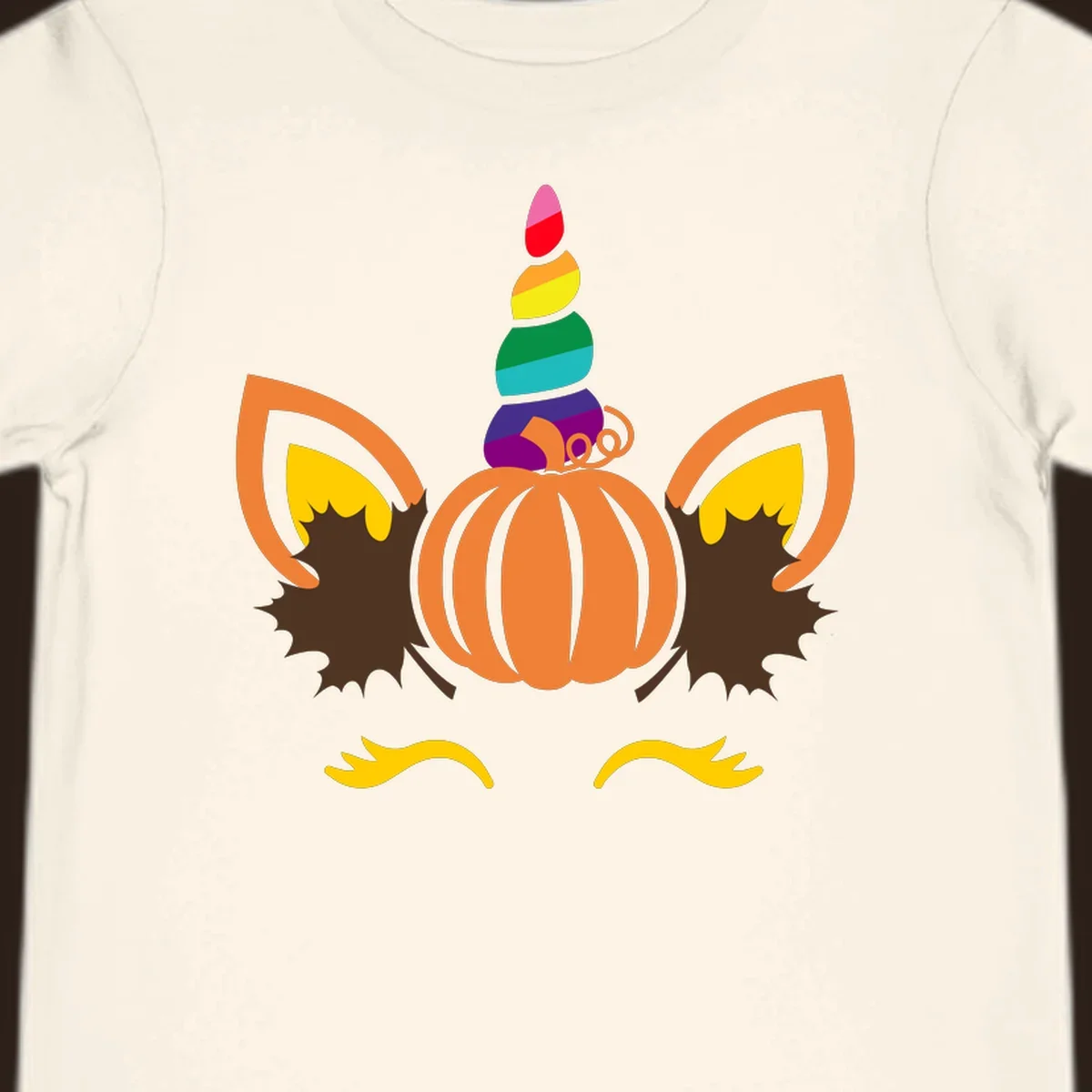 Illustration of a unicorn face made from a pumpkin with a rainbow horn and autumn leaves, on a black background.