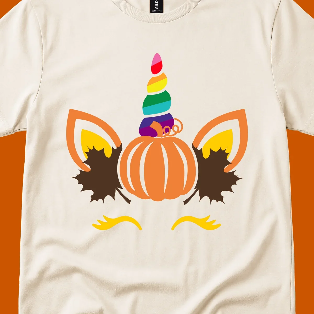 Illustration of a unicorn face made from a pumpkin with a rainbow horn and autumn leaves, on a black background.