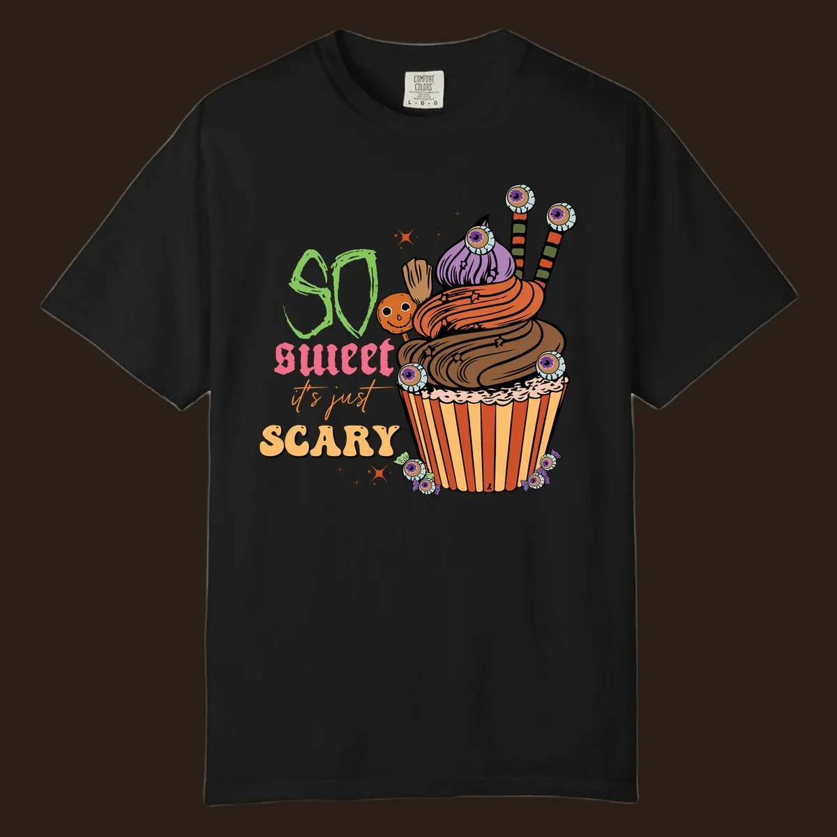 Halloween cupcake illustration with text 'So Sweet It's Just Scary', featuring candy eyeballs and a ghost lollipop.