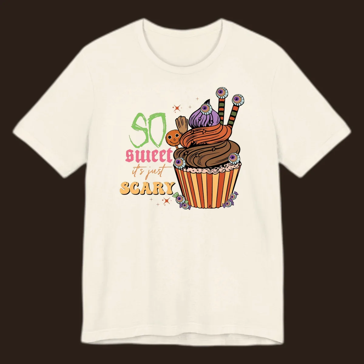 Halloween cupcake illustration with text 'So Sweet It's Just Scary', featuring candy eyeballs and a ghost lollipop.