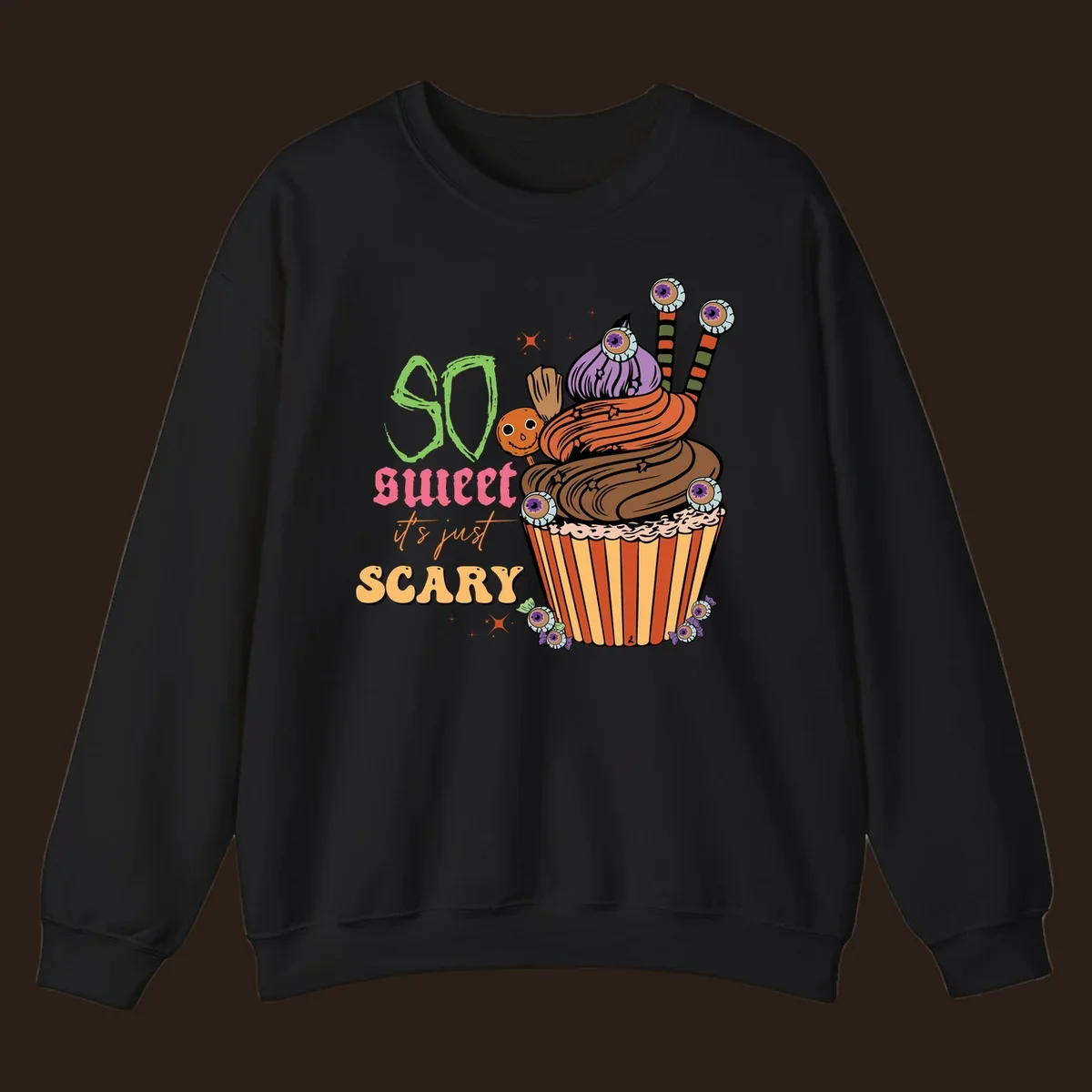Halloween cupcake illustration with text 'So Sweet It's Just Scary', featuring candy eyeballs and a ghost lollipop.