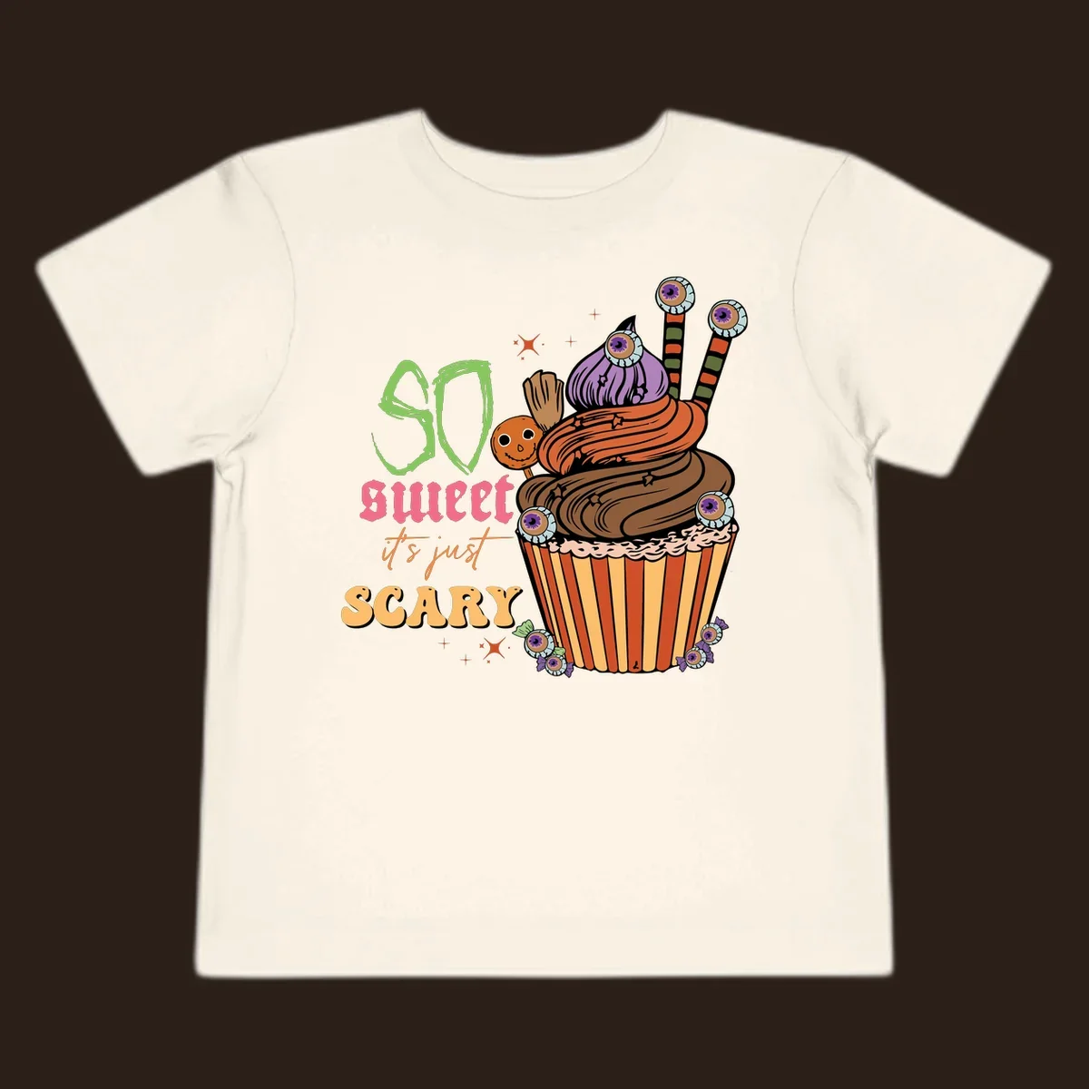 Halloween cupcake illustration with text 'So Sweet It's Just Scary', featuring candy eyeballs and a ghost lollipop.
