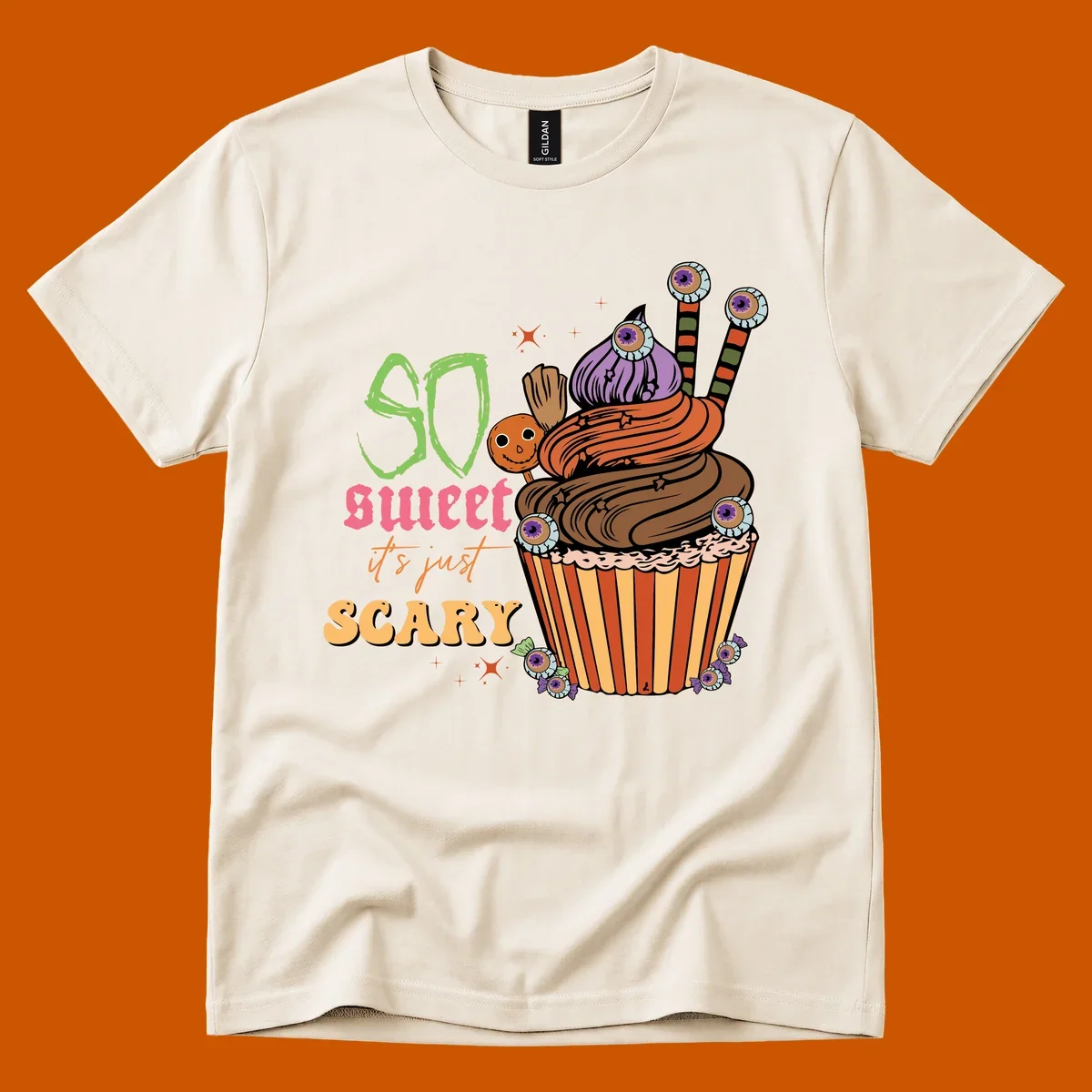 Halloween cupcake illustration with text 'So Sweet It's Just Scary', featuring candy eyeballs and a ghost lollipop.