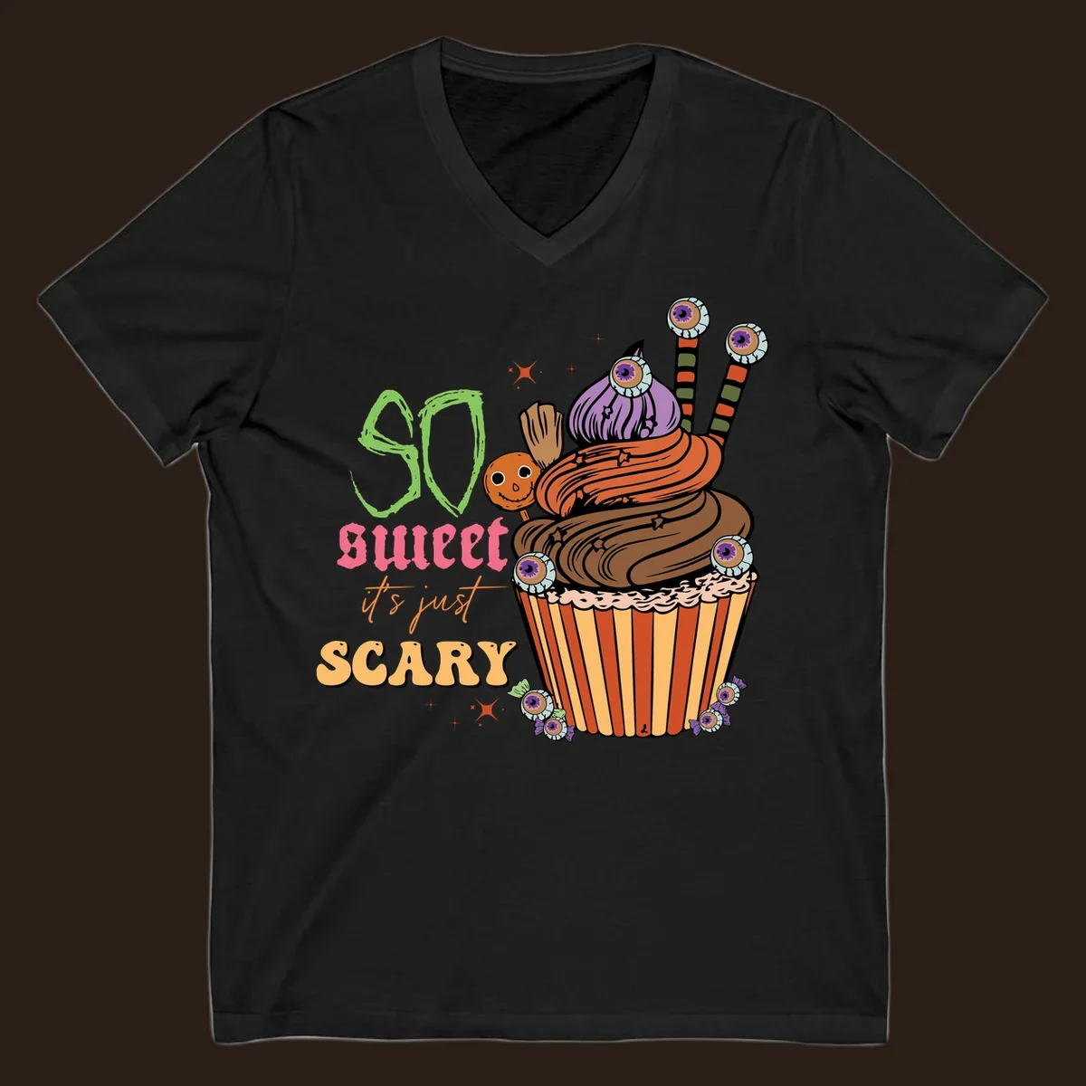 Halloween cupcake illustration with text 'So Sweet It's Just Scary', featuring candy eyeballs and a ghost lollipop.