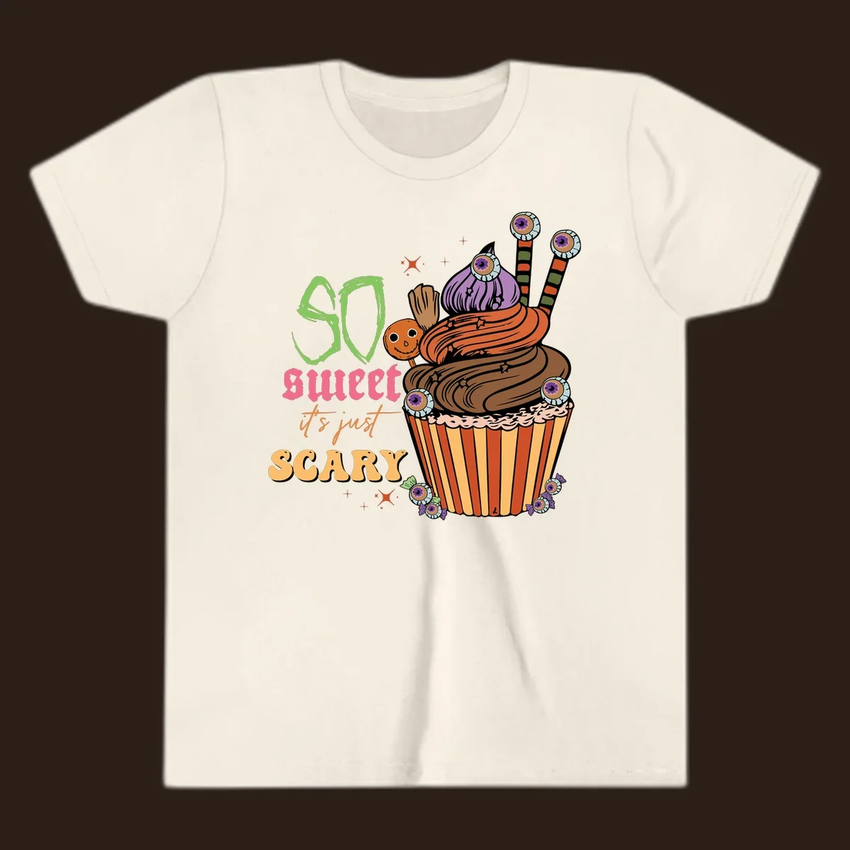 Halloween cupcake illustration with text 'So Sweet It's Just Scary', featuring candy eyeballs and a ghost lollipop.