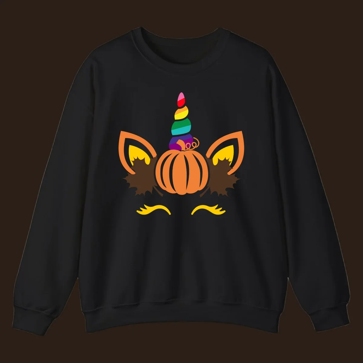 Illustration of a unicorn face made from a pumpkin with a rainbow horn and autumn leaves, on a black background.