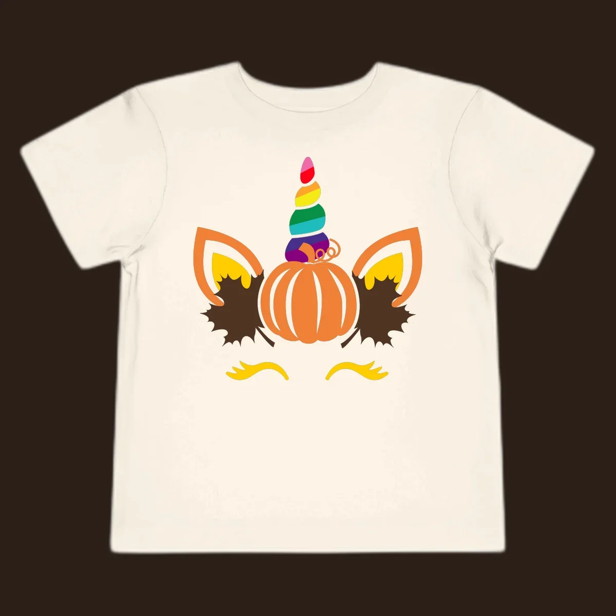 Illustration of a unicorn face made from a pumpkin with a rainbow horn and autumn leaves, on a black background.