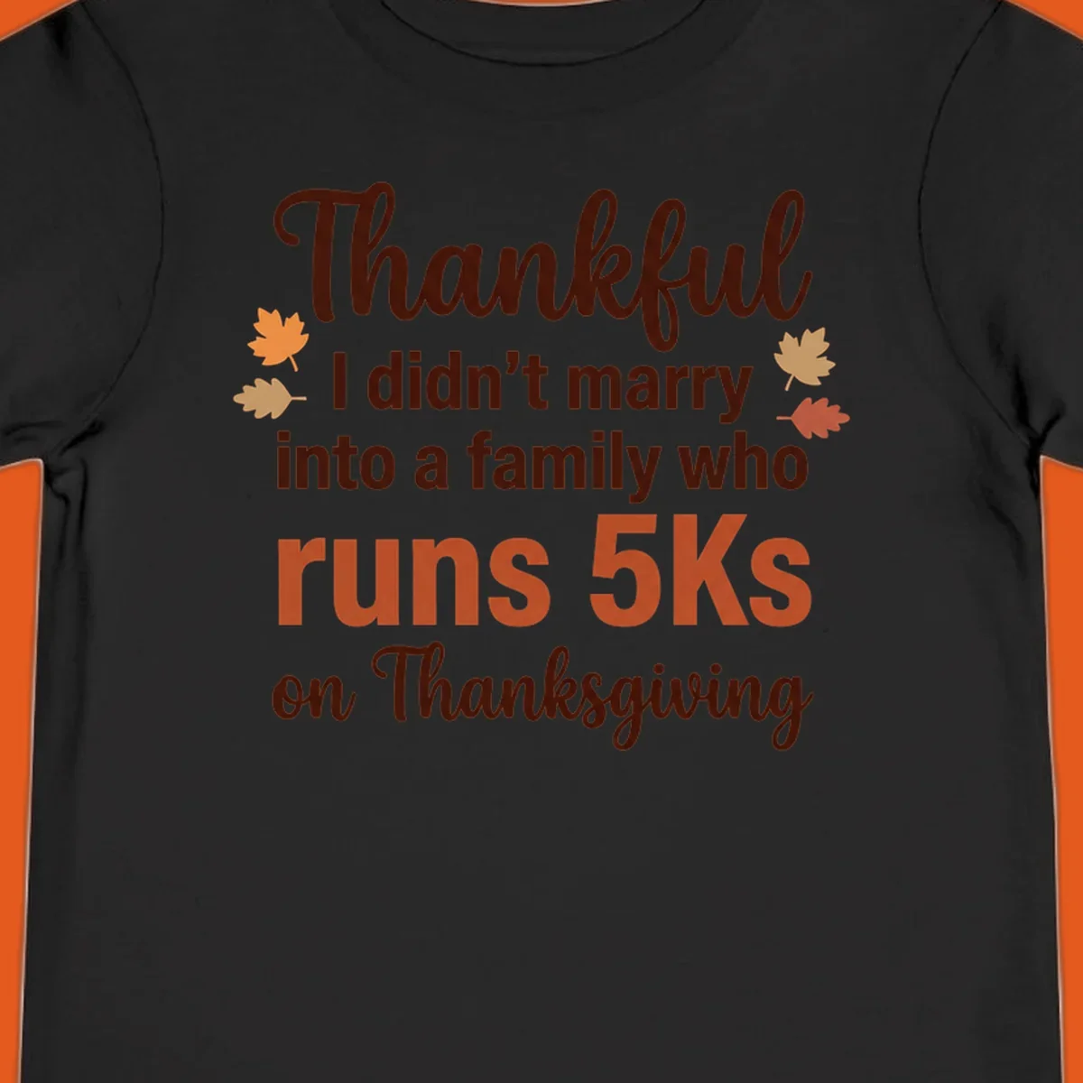 Text design 'Thankful I didn't marry into a family who runs 5Ks on Thanksgiving' with autumn leaves, for Thanksgiving 5k runner.