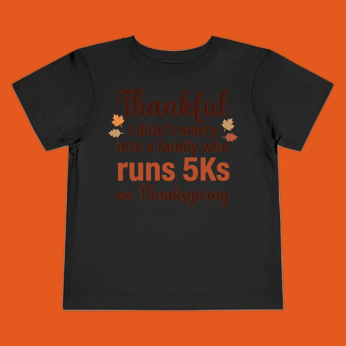 Text design 'Thankful I didn't marry into a family who runs 5Ks on Thanksgiving' with autumn leaves, for Thanksgiving 5k runner.