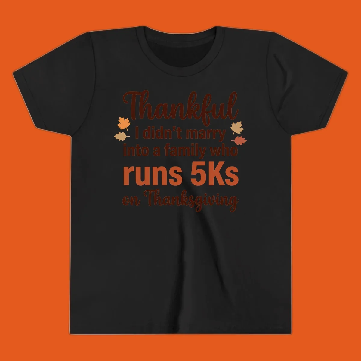 Text design 'Thankful I didn't marry into a family who runs 5Ks on Thanksgiving' with autumn leaves, for Thanksgiving 5k runner.